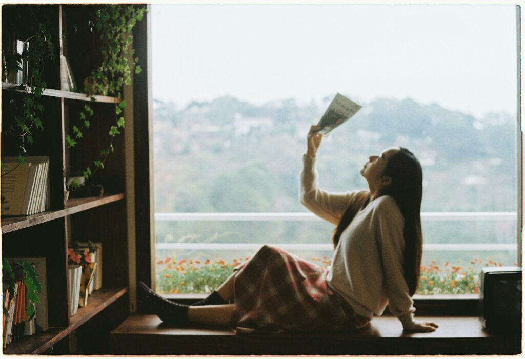 Una imagen serena de una mujer leyendo un libro mientras estaba sentada junto a una ventana con vista a las montañas.